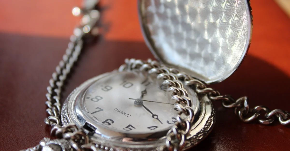 Gros plan sur une montre de poche vintage en argent avec chaîne, au design élégant.