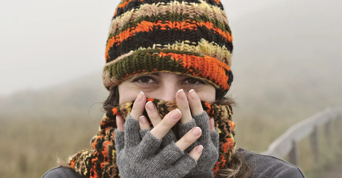 Une femme porte un bonnet tricoté et des gants dans un paysage équatorien brumeux, capturant une atmosphère hivernale chaleureuse.