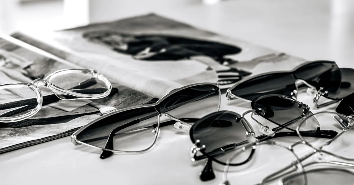Des lunettes de soleil élégantes, disposées sur la couverture d'un magazine glacé dans une composition épurée en noir et blanc.