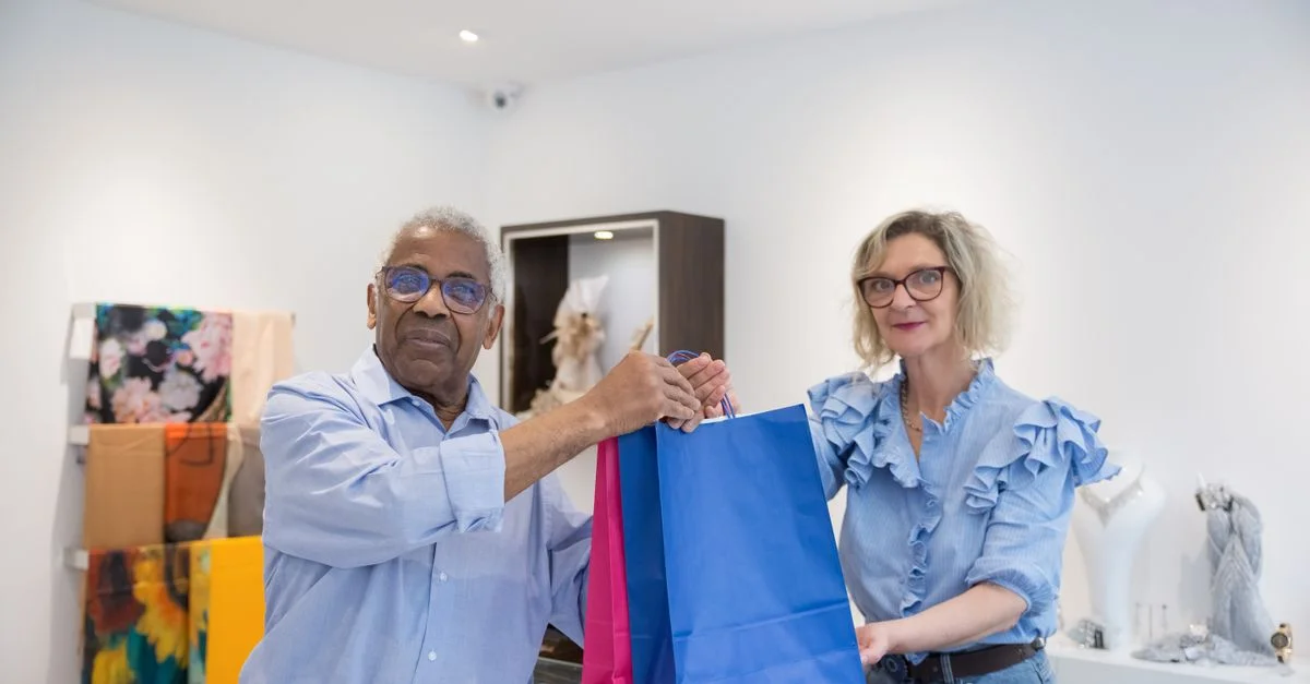 Un homme et une femme âgées faisant des courses ensemble dans un magasin de vêtements, portant des sacs colorés.